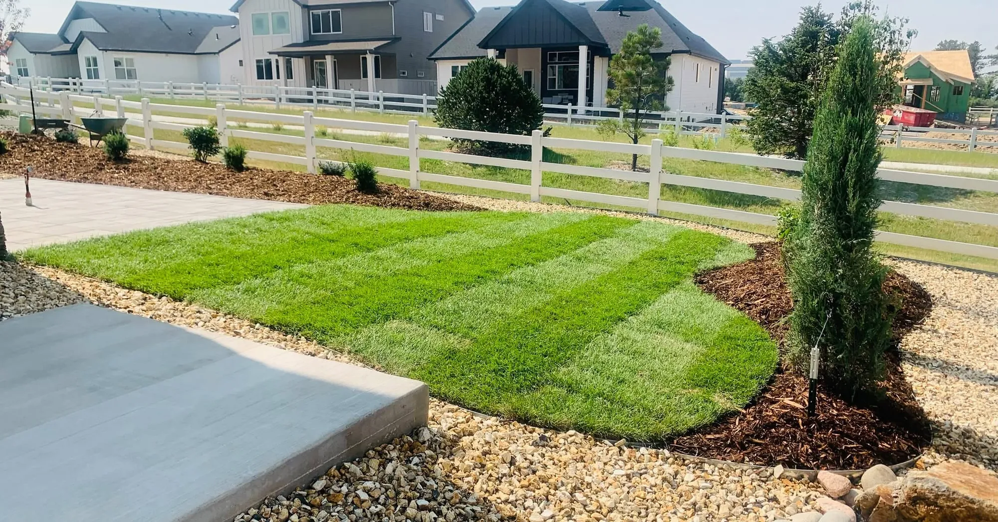 Fresh sod lawn with a mulch bed and concrete walkway beside a white fence